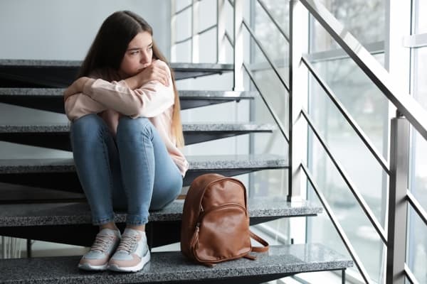 Teenager sitting alone on a staircase beside a backpack.