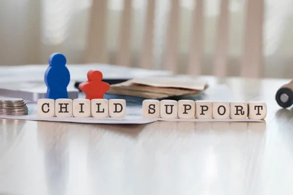Wooden blocks spelling child support with two parent figures.